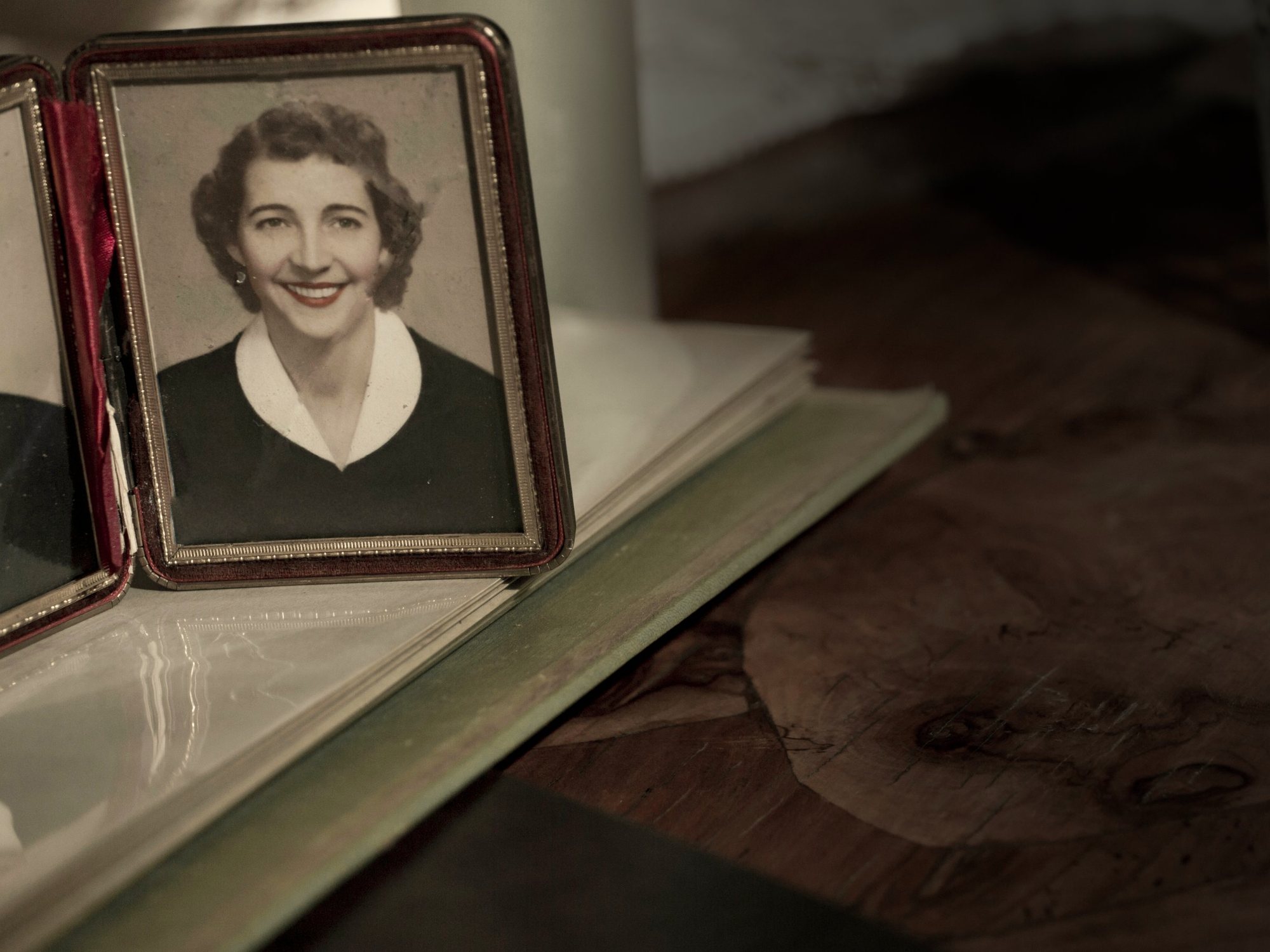 A hand-tinted 1950s portrait of a smiling woman in a folding frame, standing on an open family album