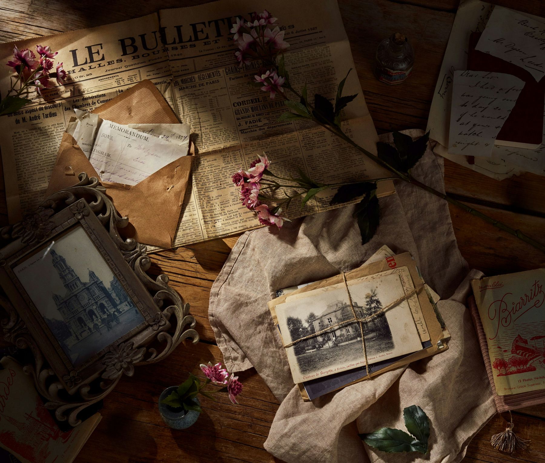 Letters, photographs, a frame and dried flowers spread across a wooden desk